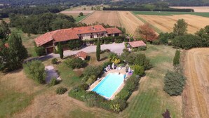 Vista aérea de una casa grande con piscina, rodeada de exuberante vegetación y campos.