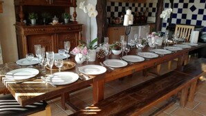 Una larga mesa de comedor dispuesta con platos, vasos y cubiertos, flanqueada por bancos.