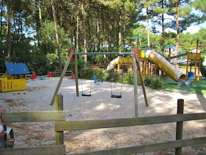 A playground with swings, a slide, and a climbing structure surrounded by trees.