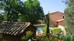 A rustic building with a tiled roof, surrounded by lush greenery and a clear blue sky.