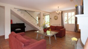A living room with a staircase, a piano, a red sofa, a glass coffee table, and a potted plant.