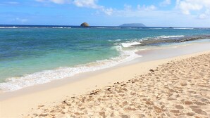 A beach with clear turquoise water, a sandy shore, and a distant island.