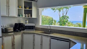 A kitchen with white cabinets, a microwave, a coffee maker, and a window with a view of the ocean.