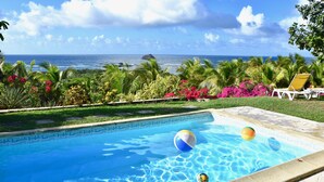 A swimming pool with clear blue water, surrounded by lush greenery and a view of the ocean.