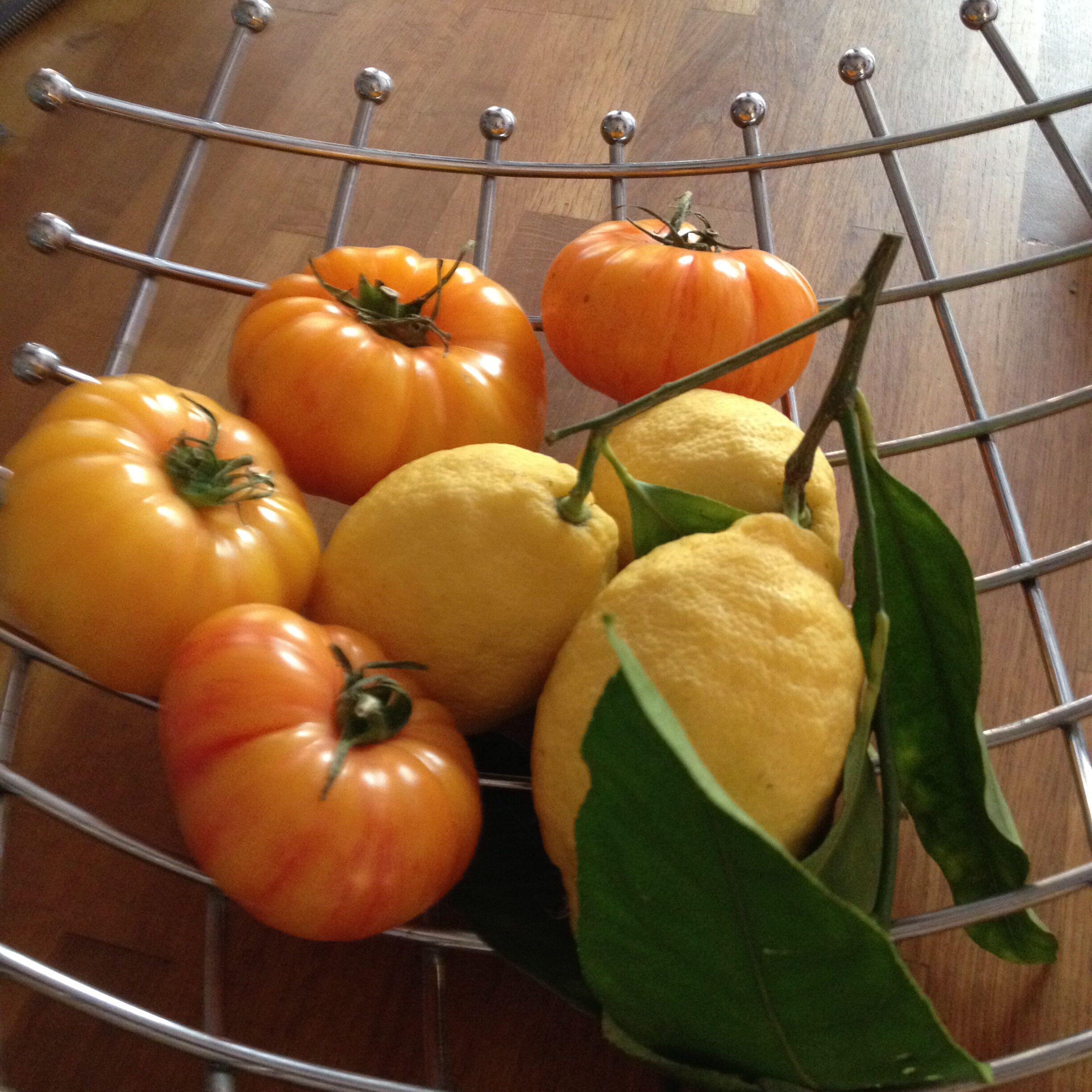 Un cesto di vimini con pomodori e limoni su un tavolo di legno.