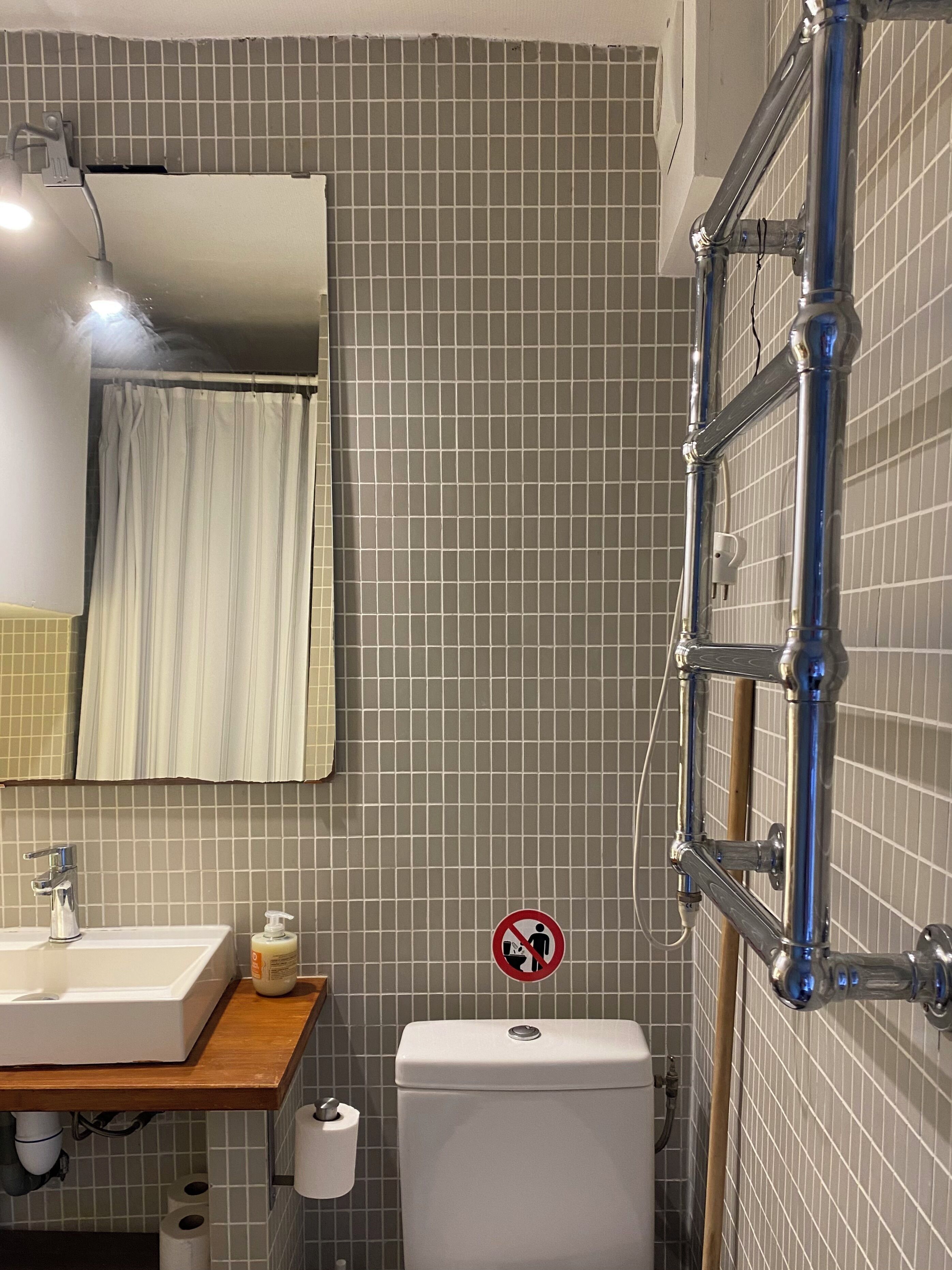 A bathroom with a sink, mirror, toilet, and a no-entry sign.