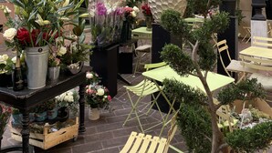 An outdoor flower shop with various plants and flowers displayed in pots and vases, set against a building with green shutters and a yellow awning. - RARE CHARMING APARTMENT IN OLD NICE, WITH A GARDEN VIEW, CLOSE TO THE SEA (Nice)