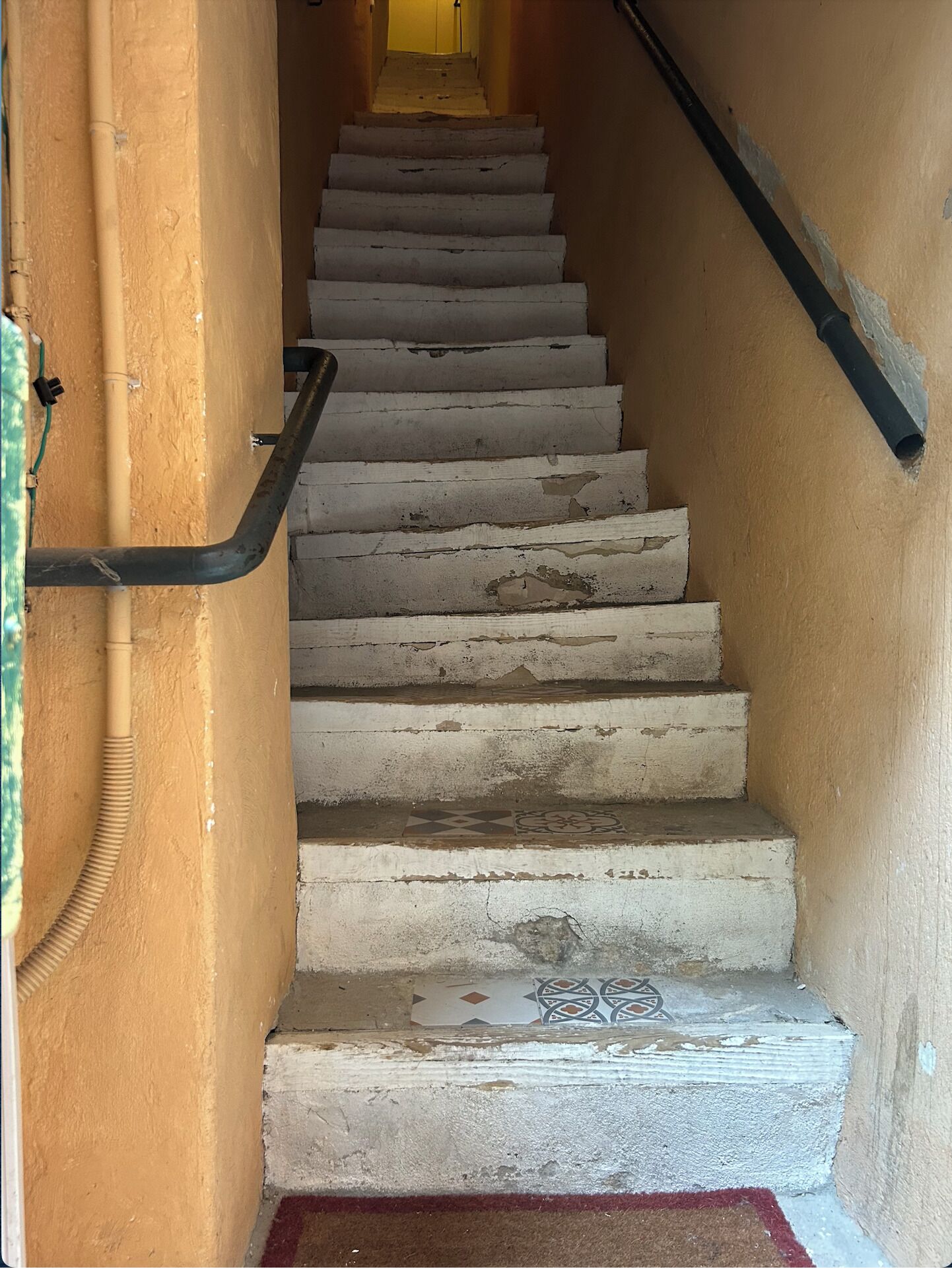 Una escalera con escalones desgastados y barandilla, que lleva a una puerta en la parte superior.