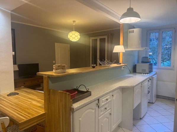 Une cuisine compacte avec une table à manger en bois, un four à micro-ondes encastré et une fenêtre donnant sur des arbres.