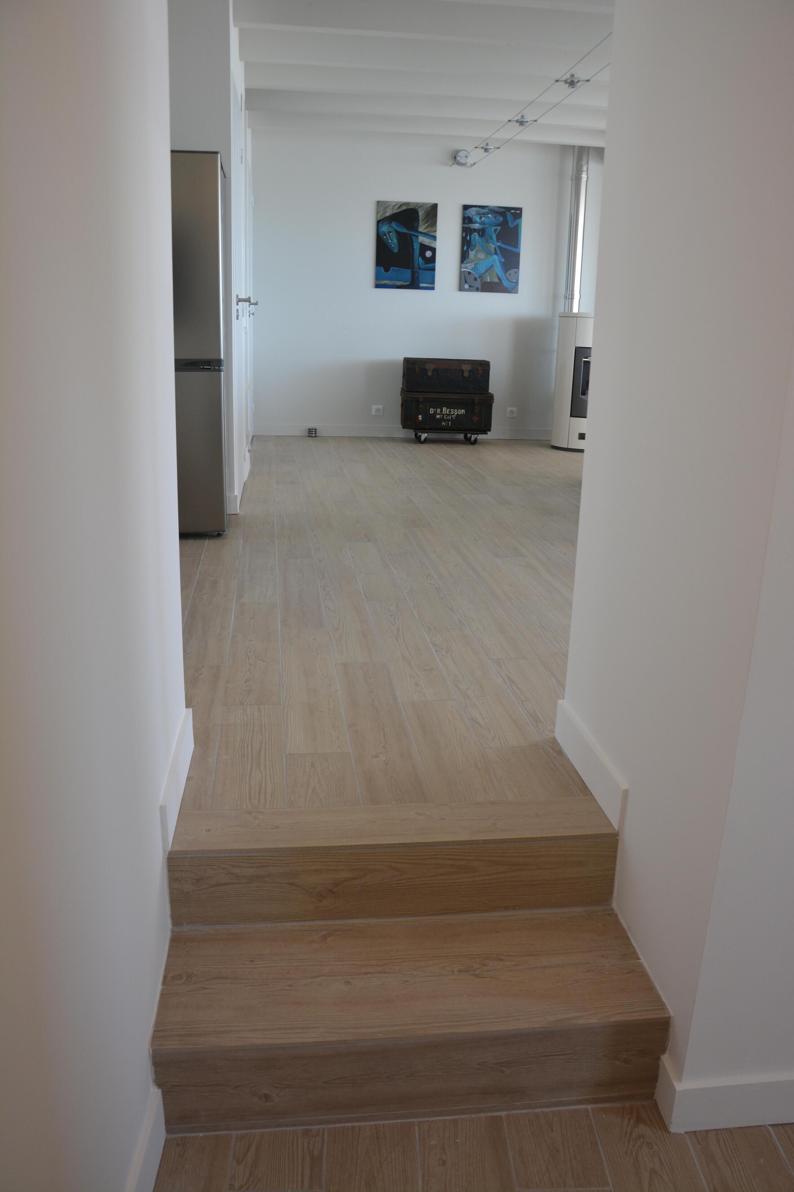 A staircase leading to a living area with a refrigerator, a suitcase, and artwork on the wall.