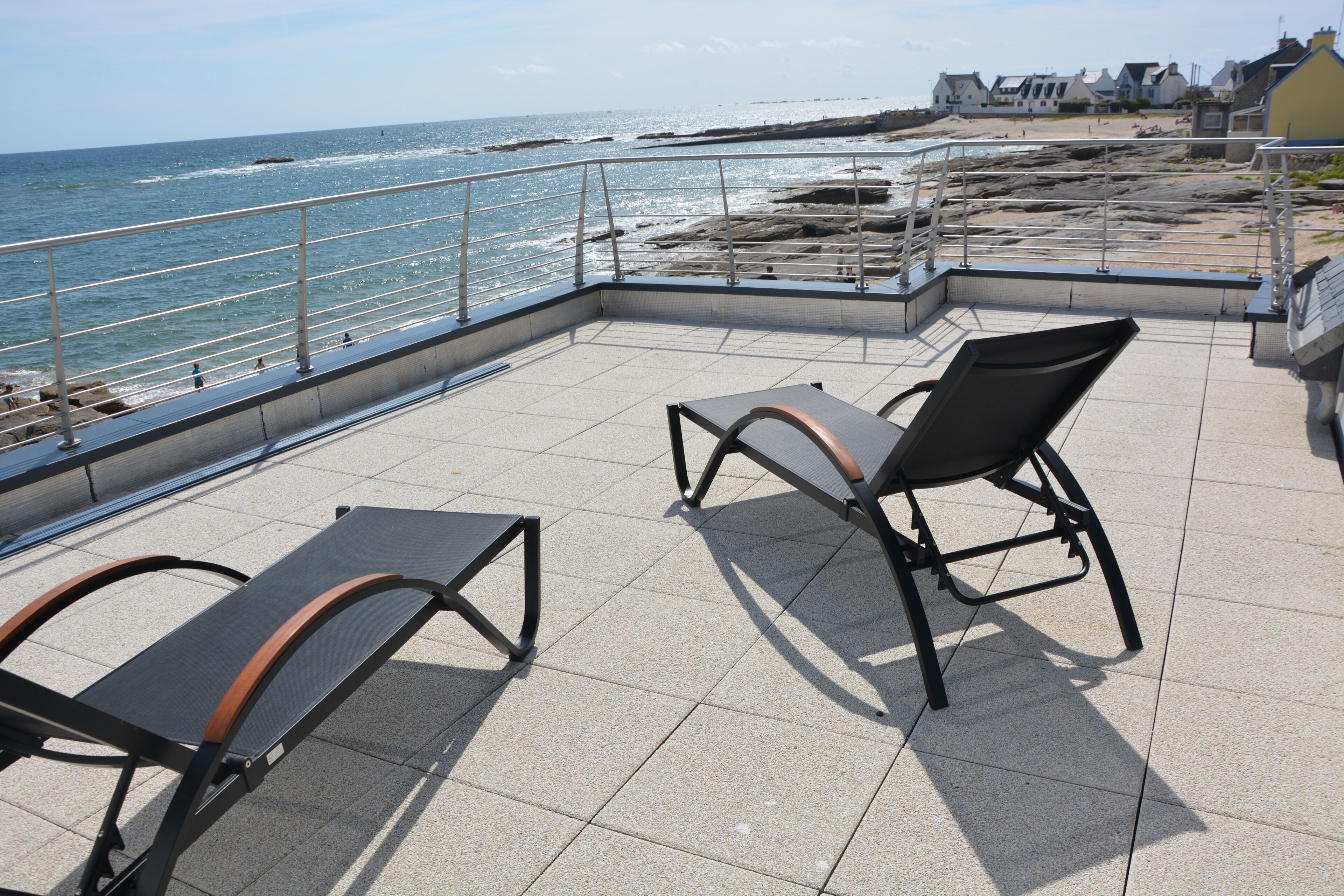 Un espace extérieur aménagé avec deux chaises et une table, offrant une vue sur une plage rocheuse et l’océan.
