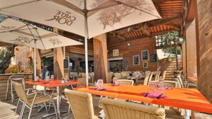 An outdoor dining area with wooden tables and wicker chairs, covered by large umbrellas with the logo "POUR DE L'EAU". - Cap Esterel (St Raphaël) - Quiet apartment with sea view, golf & Cap Esterel 4 pers. (Saint-Raphaël)
