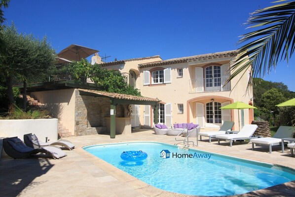 A two-story building with a swimming pool, outdoor seating, and a pergola.