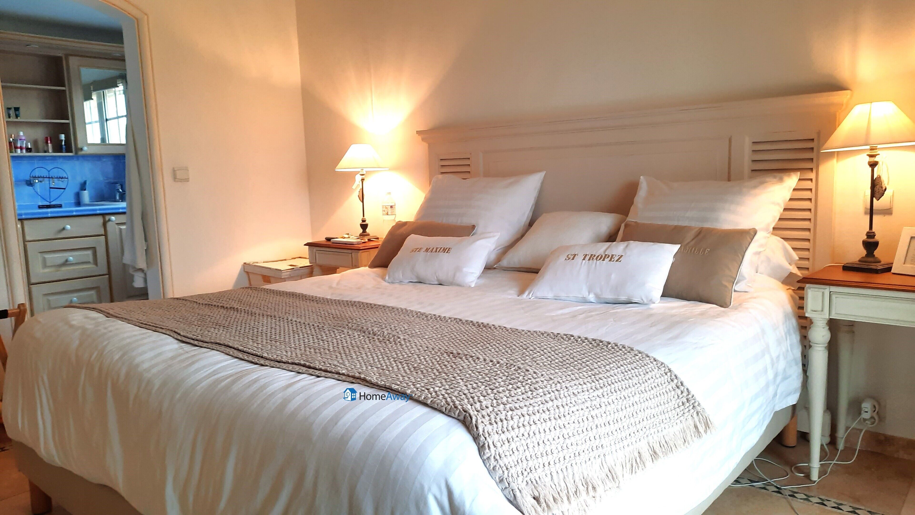 A neatly made bed with a knitted throw, two bedside lamps, and pillows with text.