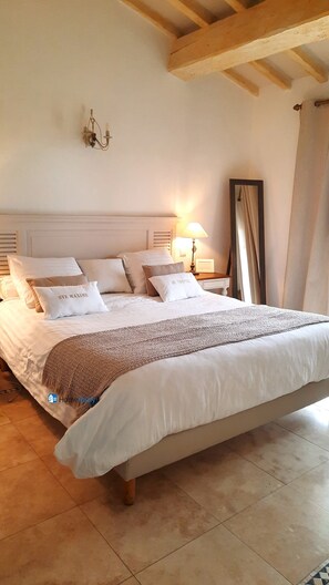 Een groot bed met witte lakens en een bruine plaid, een nachtkastje met een lamp, en een spiegel aan de muur.