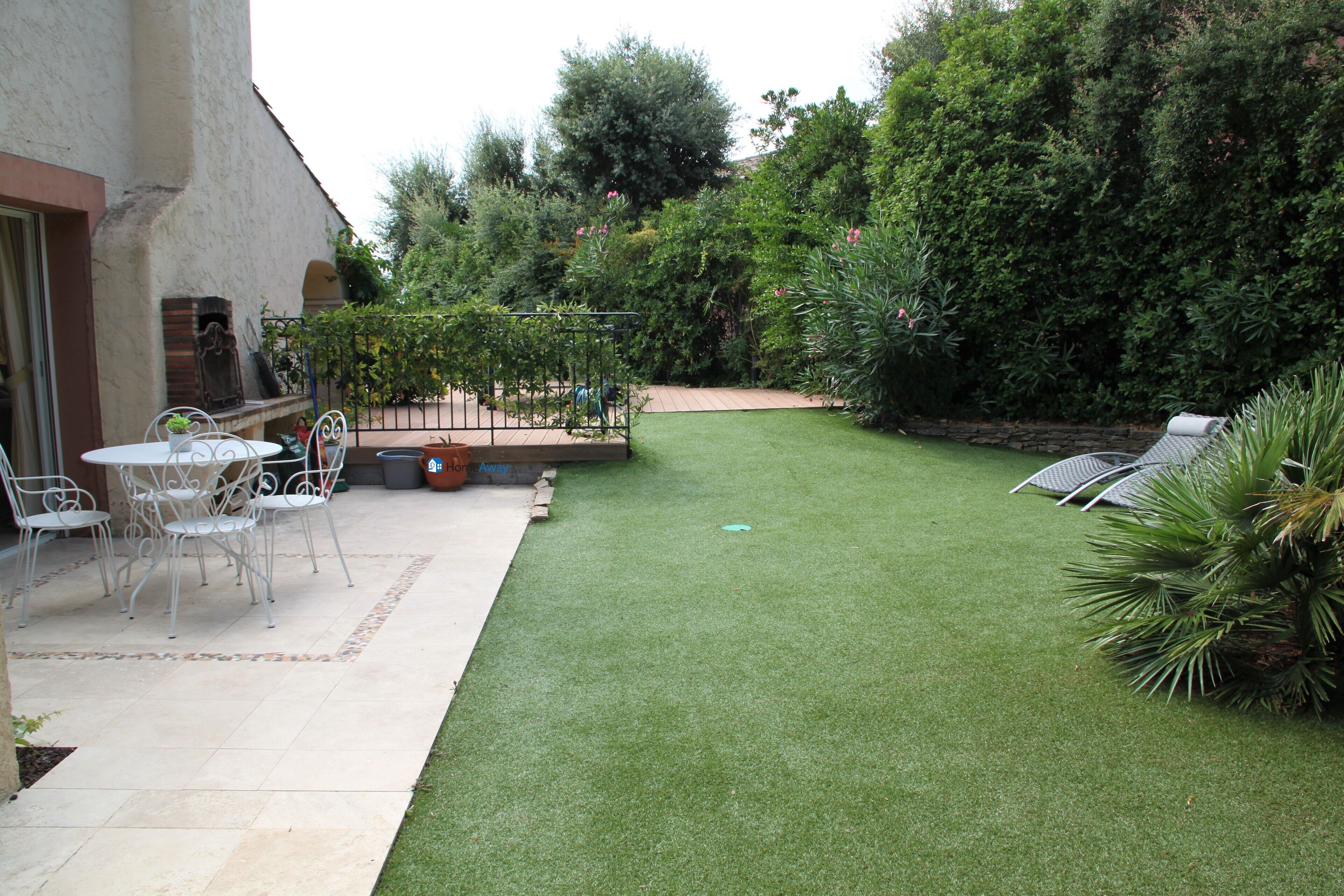 A patio area with a table and chairs, a small garden with artificial grass, and a variety of plants and trees.