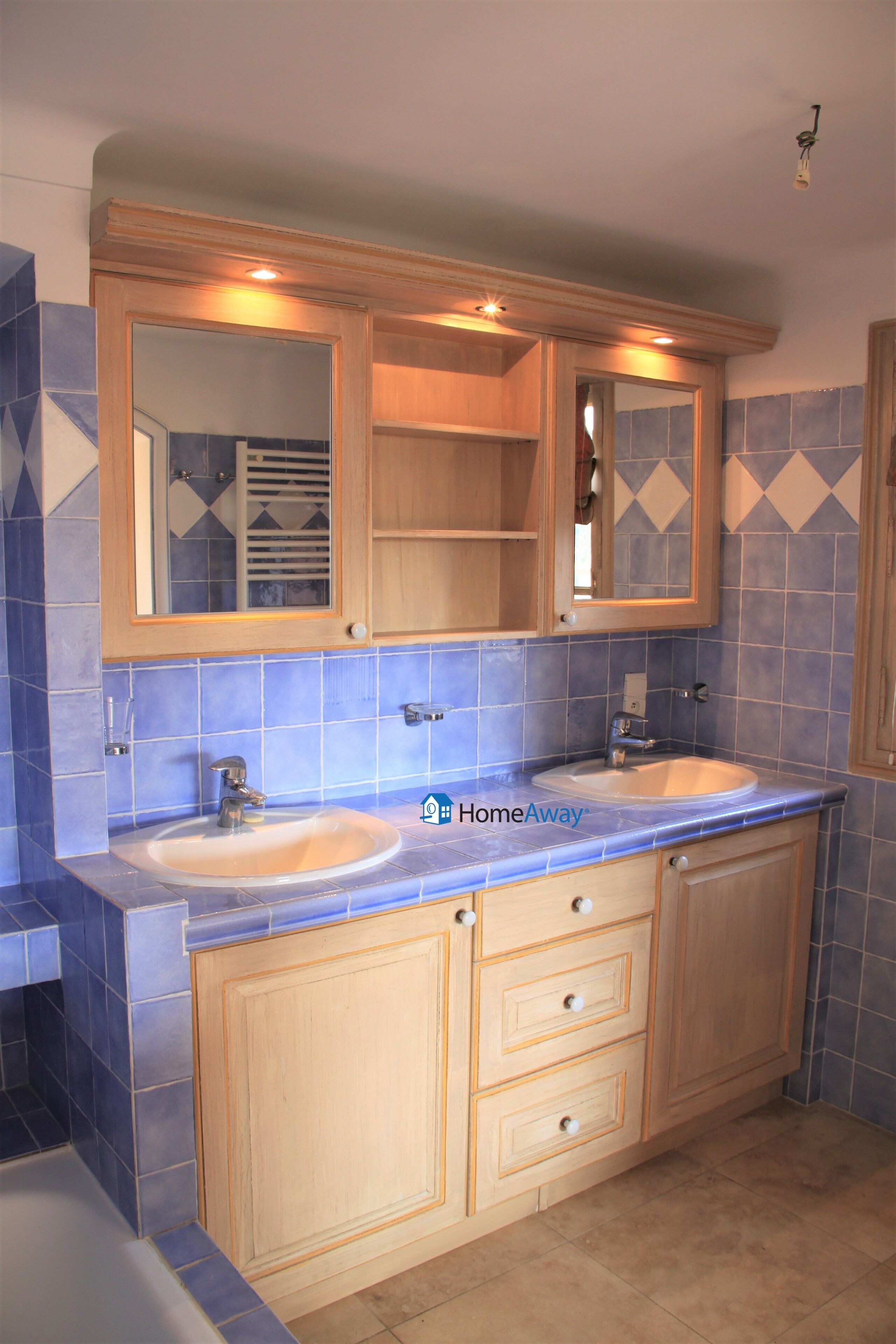 Un baño con dos lavabos, armarios de madera y paredes con azulejos azules.