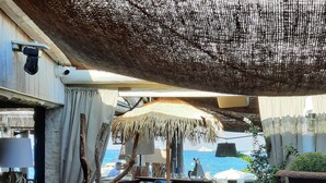Un espace extérieur aménagé avec des sièges, un parasol en chaume, du mobilier en bois et une vue sur la mer.
