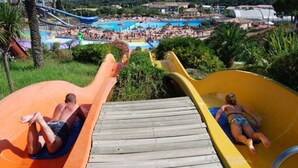 Deux toboggans aquatiques dans un complexe hôtelier, avec une piscine et une plage en arrière-plan.