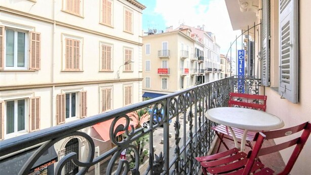 En balkon med et bord og stole, gelænder og bygninger i baggrunden.