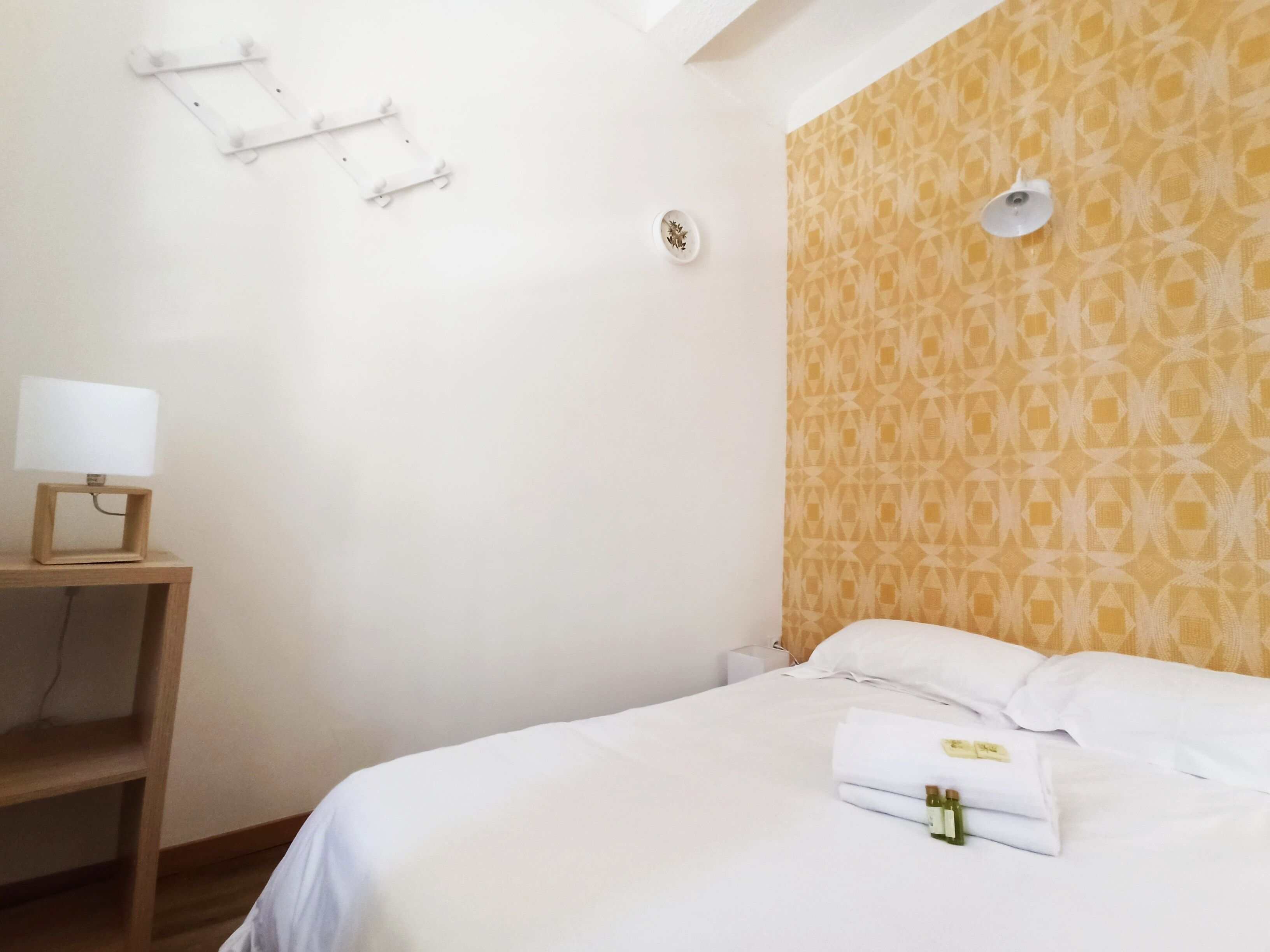 Ein Hotelzimmer mit einem Bett, einem Nachttisch mit Lampe, einer Wand mit Muster und einem kleinen Regal.