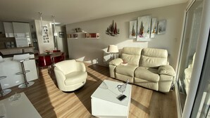 Una sala de estar moderna con un sofá color beige, una mesa de centro blanca y un comedor con una silla roja.