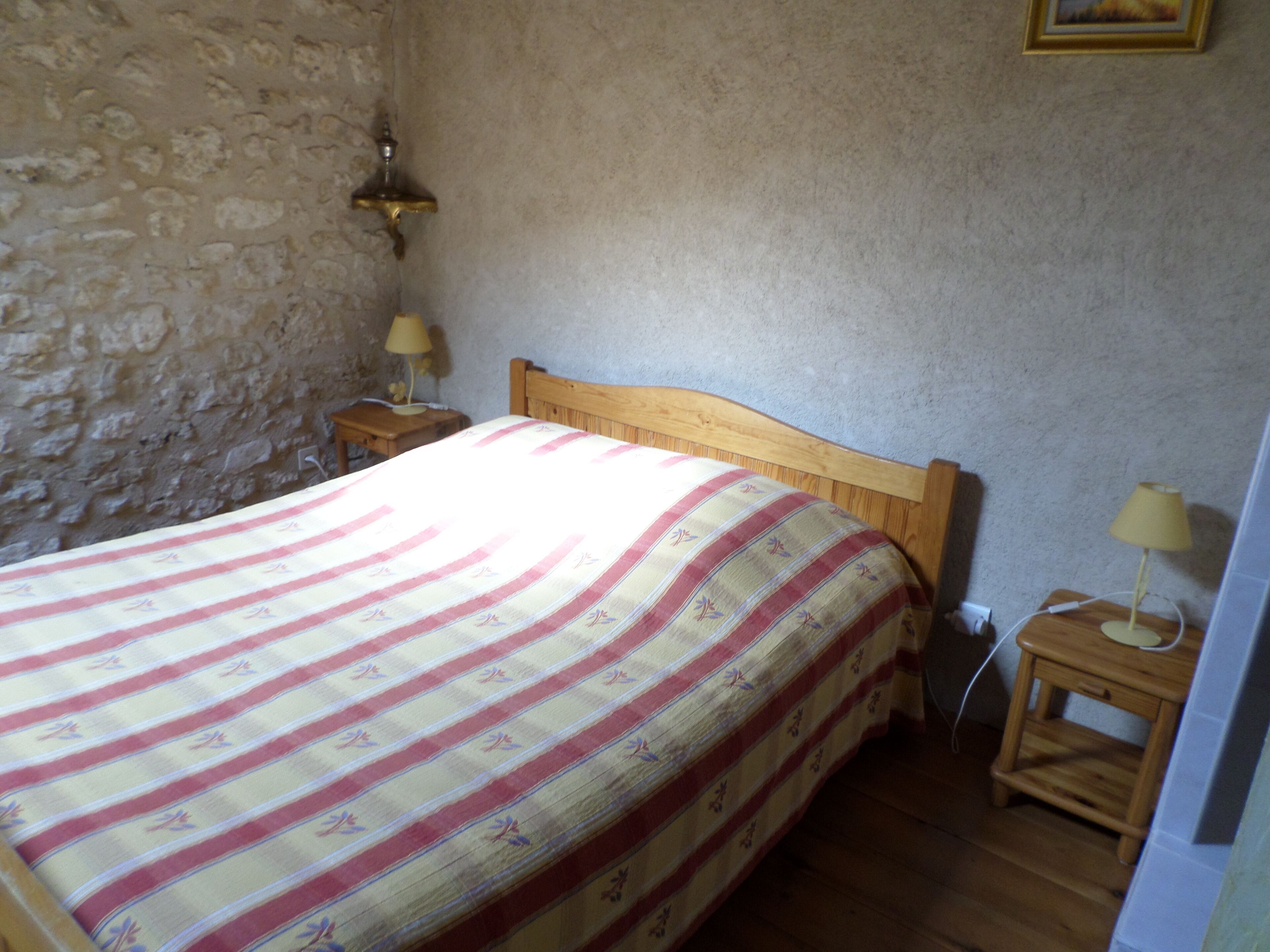 A bedroom with a wooden bed, two bedside tables with lamps, a stone wall, and a plain ceiling.
