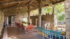 A rustic outdoor dining area with stone walls, wooden beams, and a mix of metal and plastic chairs. - Charming gîte well restored real comfort (Paulhiac)