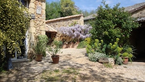 A stone building with a gravel courtyard, surrounded by various plants and trees. - Charming gîte well restored real comfort (Paulhiac)