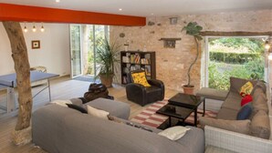A living room with a sofa, armchair, and a bookshelf. There is a dining table and chairs in the background. - Charming gîte well restored real comfort (Paulhiac)