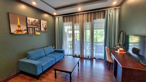 Un salon avec un canapé bleu, une table basse en bois et un bureau avec un miroir. Quatre tableaux encadrés ornent le mur, et une grande fenêtre est agrémentée de rideaux.