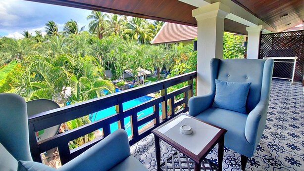 Un balcon avec des chaises bleues et une petite table, donnant sur une piscine et une végétation luxuriante.