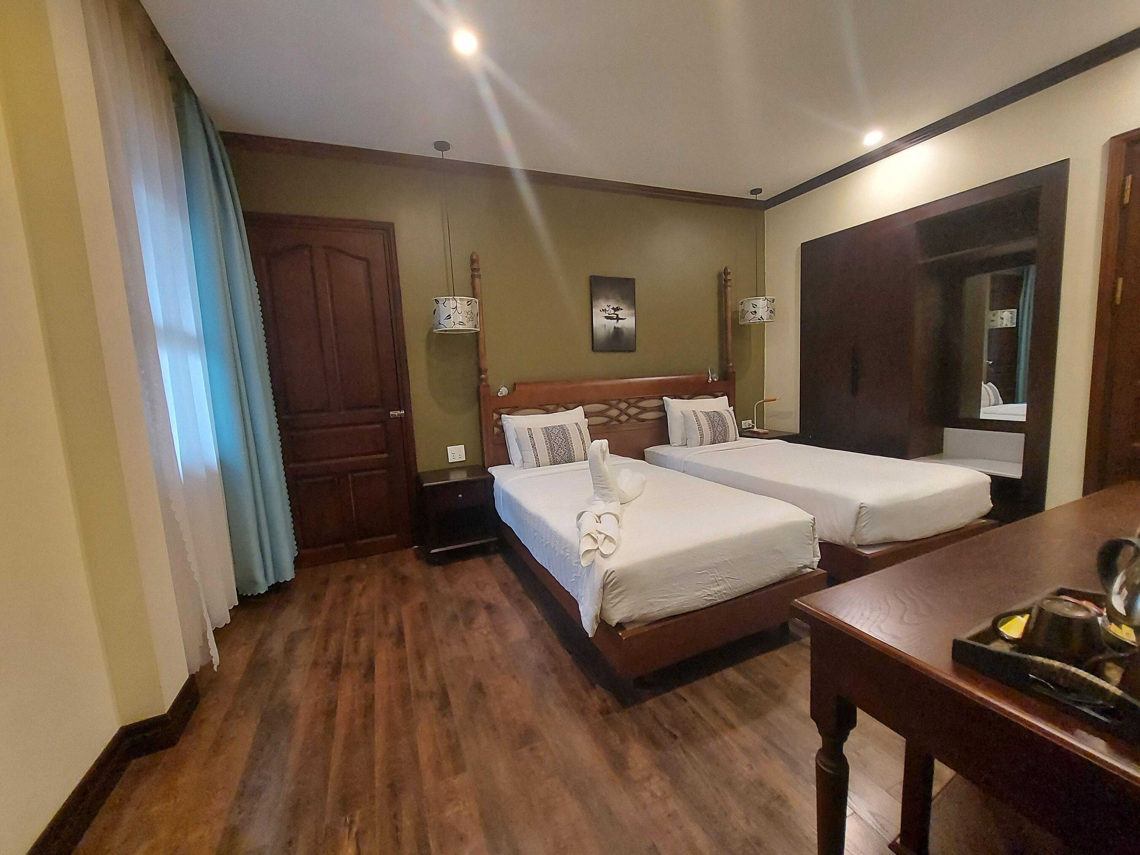 A hotel room with two beds, a wooden floor, a desk with a tray, and a mirror.