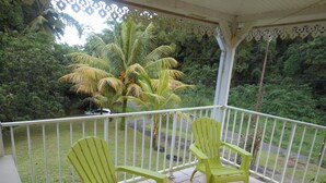 A covered balcony with two green chairs, a white railing, and a view of a road and greenery. - Villa F3 in SAINTE-MARIE (SAINTE-MARIE)