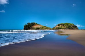 A beach with clear blue water, sandy shore, and two small hills with greenery. - Villa F3 in SAINTE-MARIE (SAINTE-MARIE)