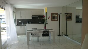 Una cocina moderna con armarios blancos, una mesa de comedor con dos sillas, un florero con flores y una lámpara de pie.
