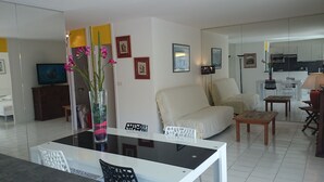 Una sala de estar moderna con una mesa de comedor de cristal, un sofá blanco y un televisor sobre un mueble bajo.