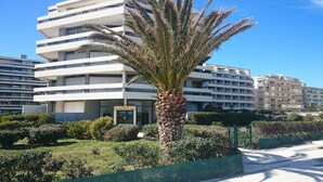 Un edificio moderno de varios pisos con balcones, rodeado de vegetación cuidada y una palmera.