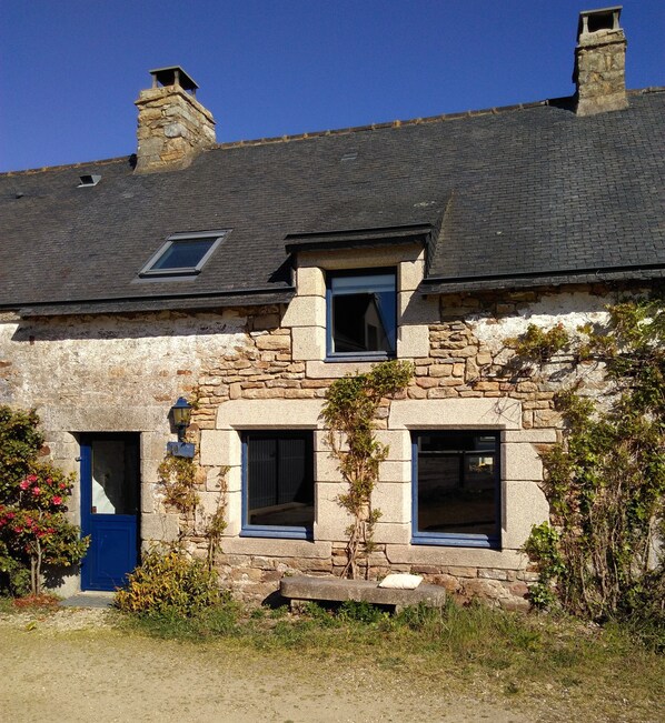 A stone house with a blue door, two windows, and a chimney.