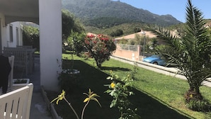 Un balcón con vista a un césped cuidado, un árbol pequeño y una montaña distante.