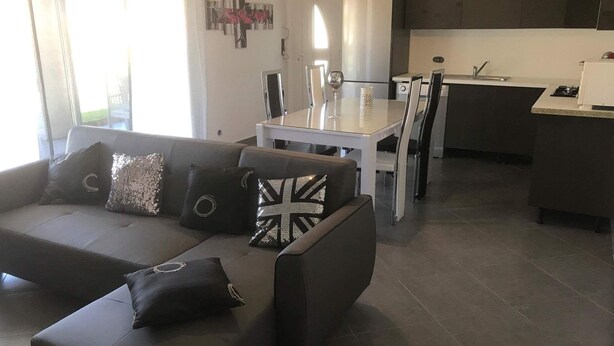 Una sala de estar moderna con un sofá de color oscuro, una mesa de comedor y una zona de cocina.