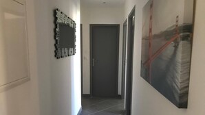 Un pasillo con suelo de baldosas, una puerta al final y un cuadro en la pared derecha.