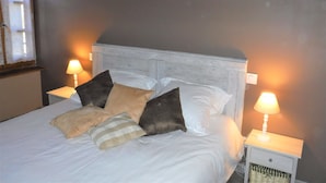 Una cama con ropa de cama blanca, varios almohadones y dos lámparas de noche.