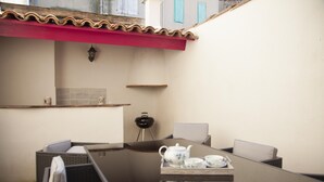 Un espacio exterior moderno para comer con mesa de vidrio, sillas de mimbre y techo rojo.