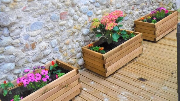 Un muro de piedra con jardineras de madera que contienen flores.