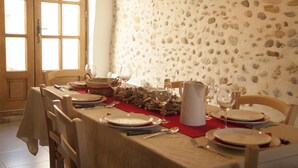 Una mesa de comedor dispuesta con platos, vasos y cubiertos, con una pared de piedra y una puerta de madera al fondo.