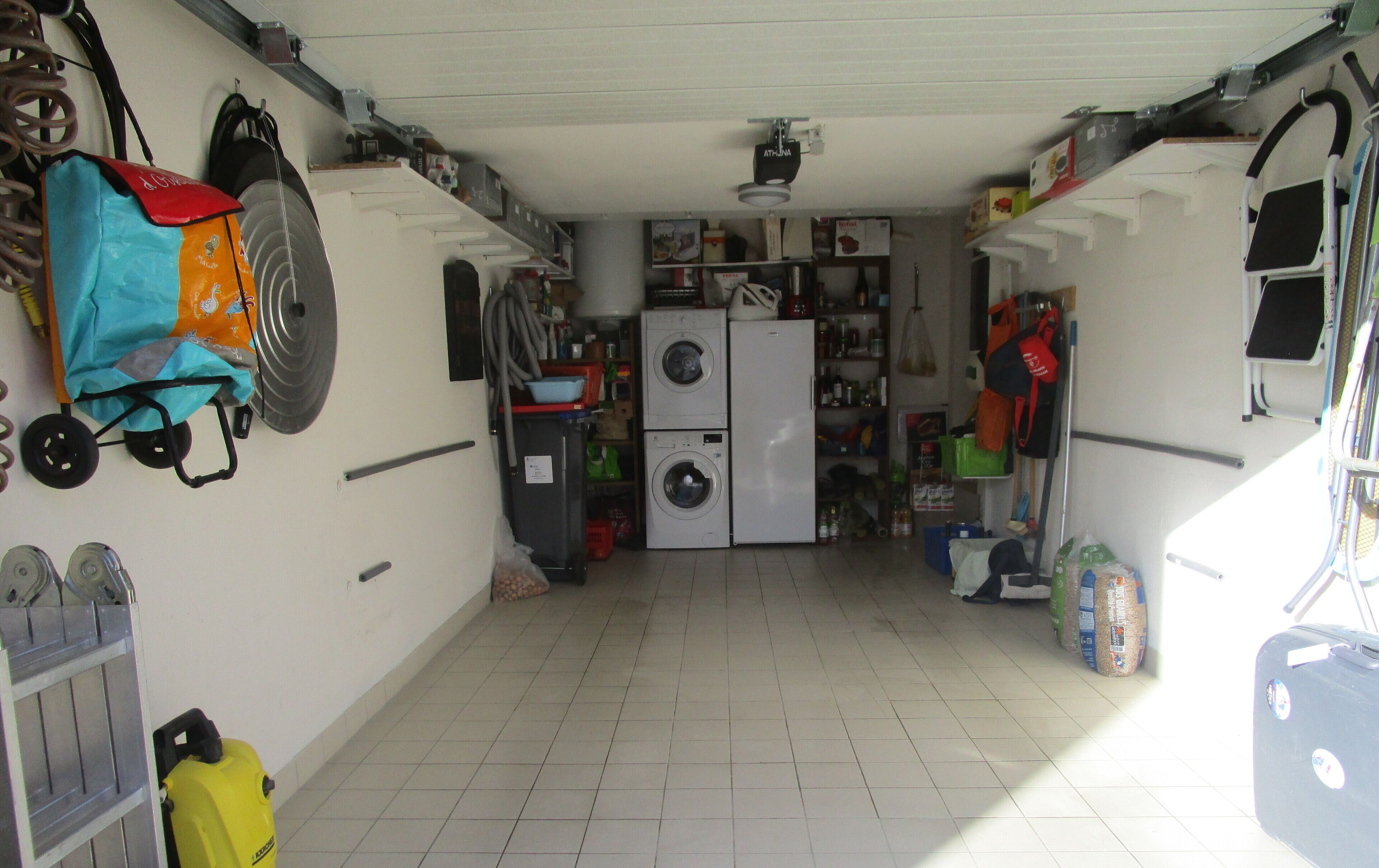 Een kleine, overzichtelijke wasruimte met een wasmachine, droger en diverse schoonmaakmiddelen.