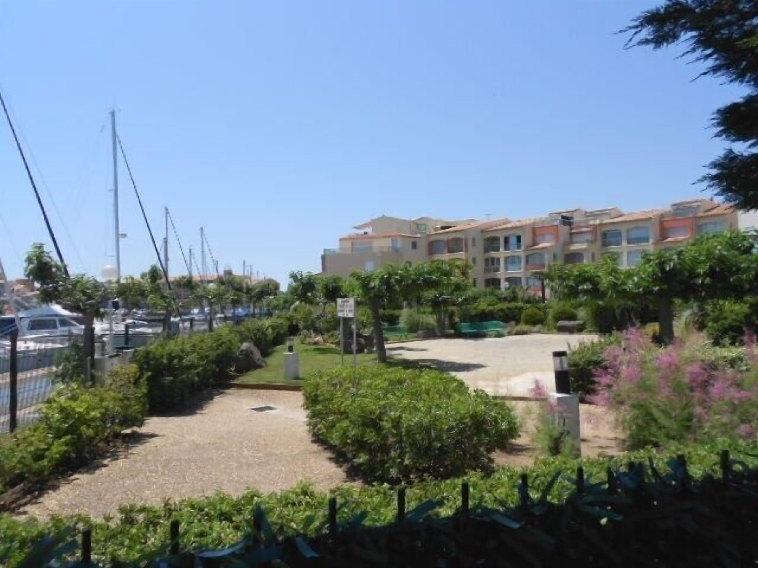 A marina with boats, a parking area, and a row of multi-story buildings with balconies.