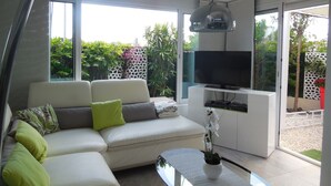 En moderne stue med en hvid sofa, grønne puder, et fladskærms-tv og en orkidé i potte.