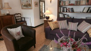 A living room with a brown leather armchair, a purple sofa, a glass coffee table, a bookshelf, a lamp, and a painting on the wall. - Nice spacious village house and sunny downtown (Saint-Rémy-De-Provence)